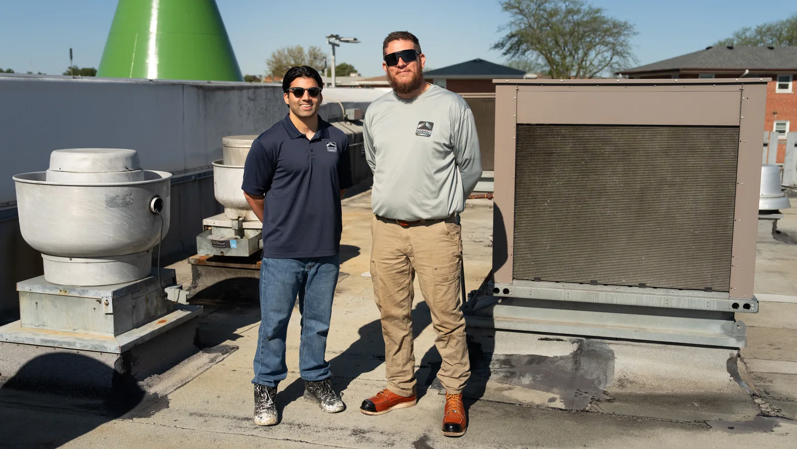 Two RoofingSource teammates standing between rooftop units on a commercial roof