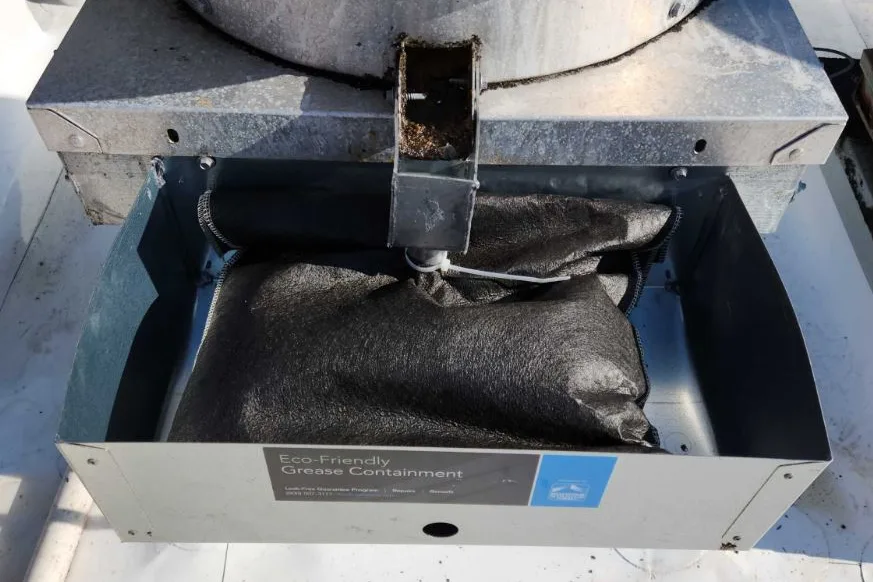 A grease containment unit fitted beneath a rooftop ventilator, absorbent in place