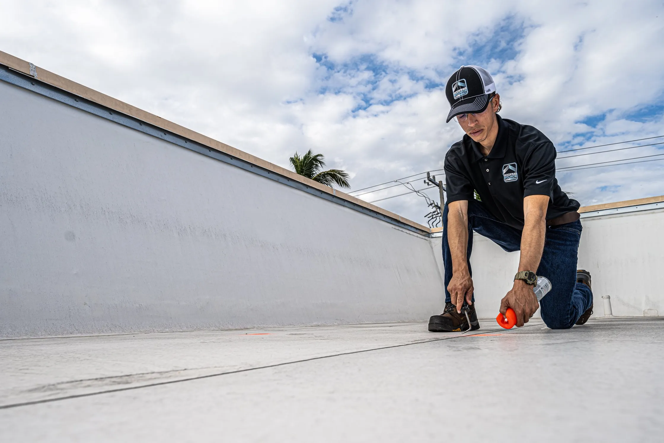 A RoofingSource team member kneeling on a roof, marking a seam