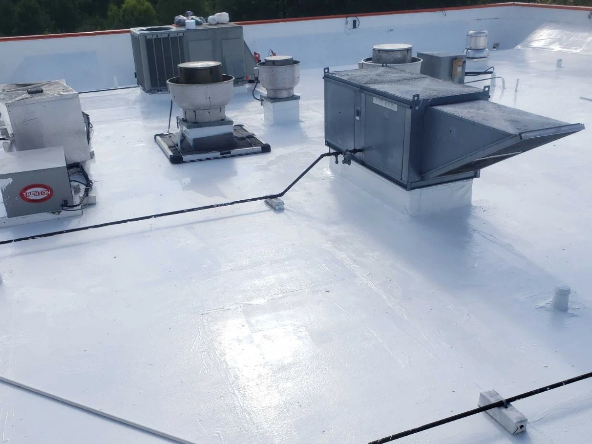A commercial roof under a fresh white reflective coating, its rooftop units and curbs coated with it