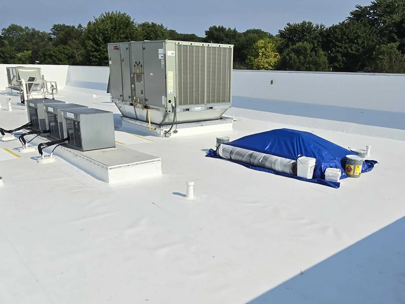 A completed white commercial roof, a roll of membrane and its materials still staged on the deck