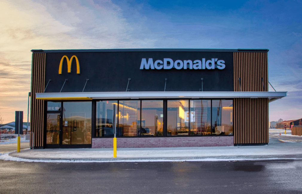 A McDonald’s restaurant at dusk, its lit sign and arches above the storefront windows.