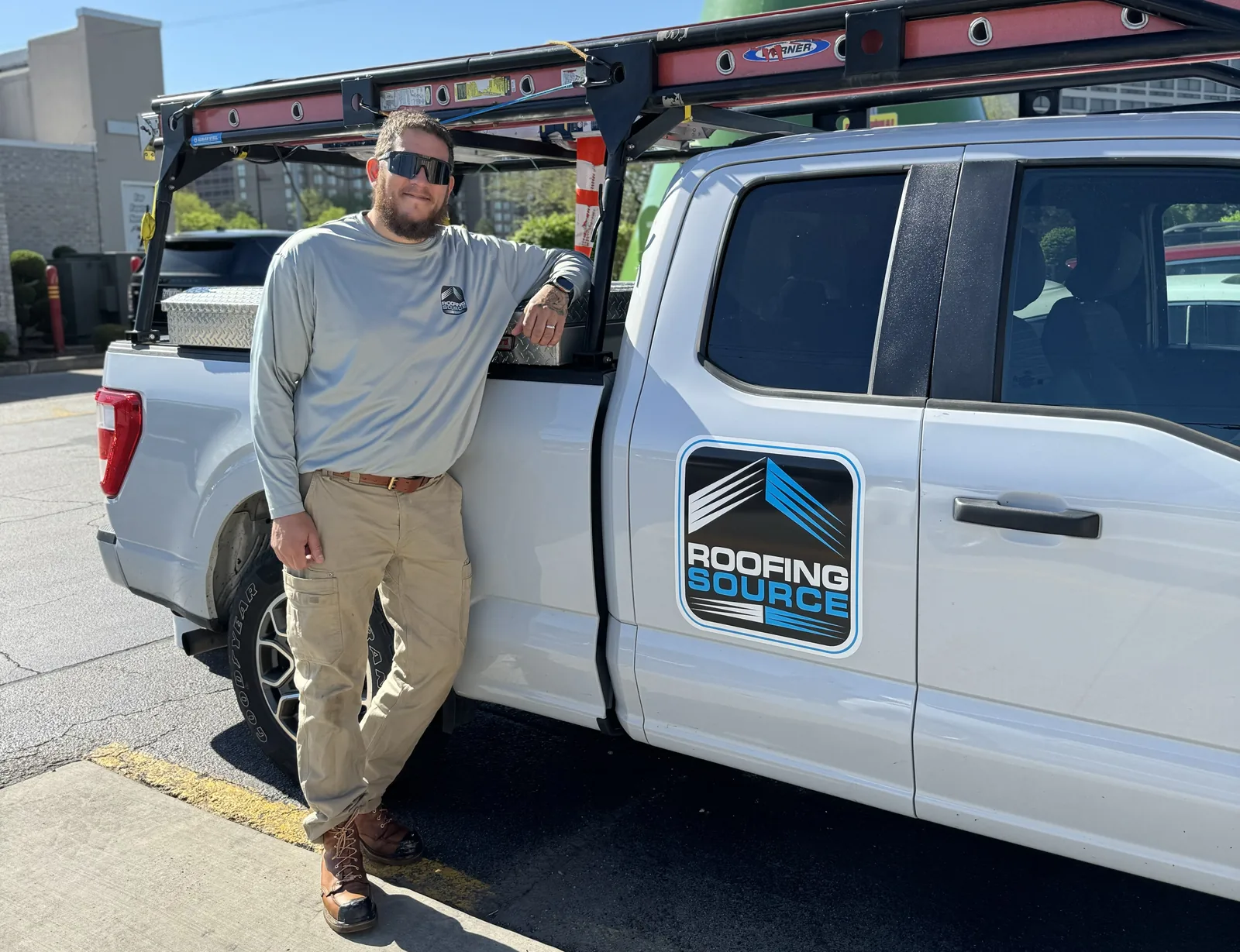 A RoofingSource teammate leaning on a RoofingSource service truck with a ladder rack