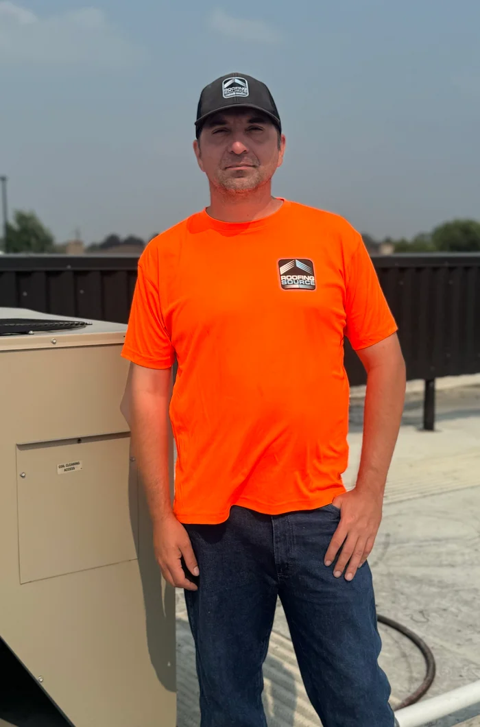 A RoofingSource teammate in an orange shirt and company cap on a commercial roof