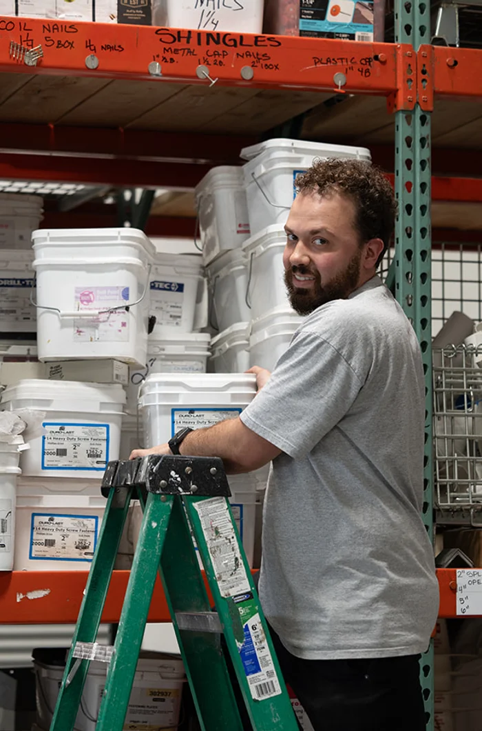 A RoofingSource teammate on a ladder in the headquarters supply warehouse