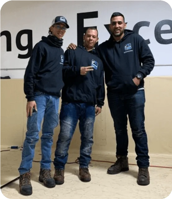 Tres compañeros frente al letrero Maintaining Excellence en la sede