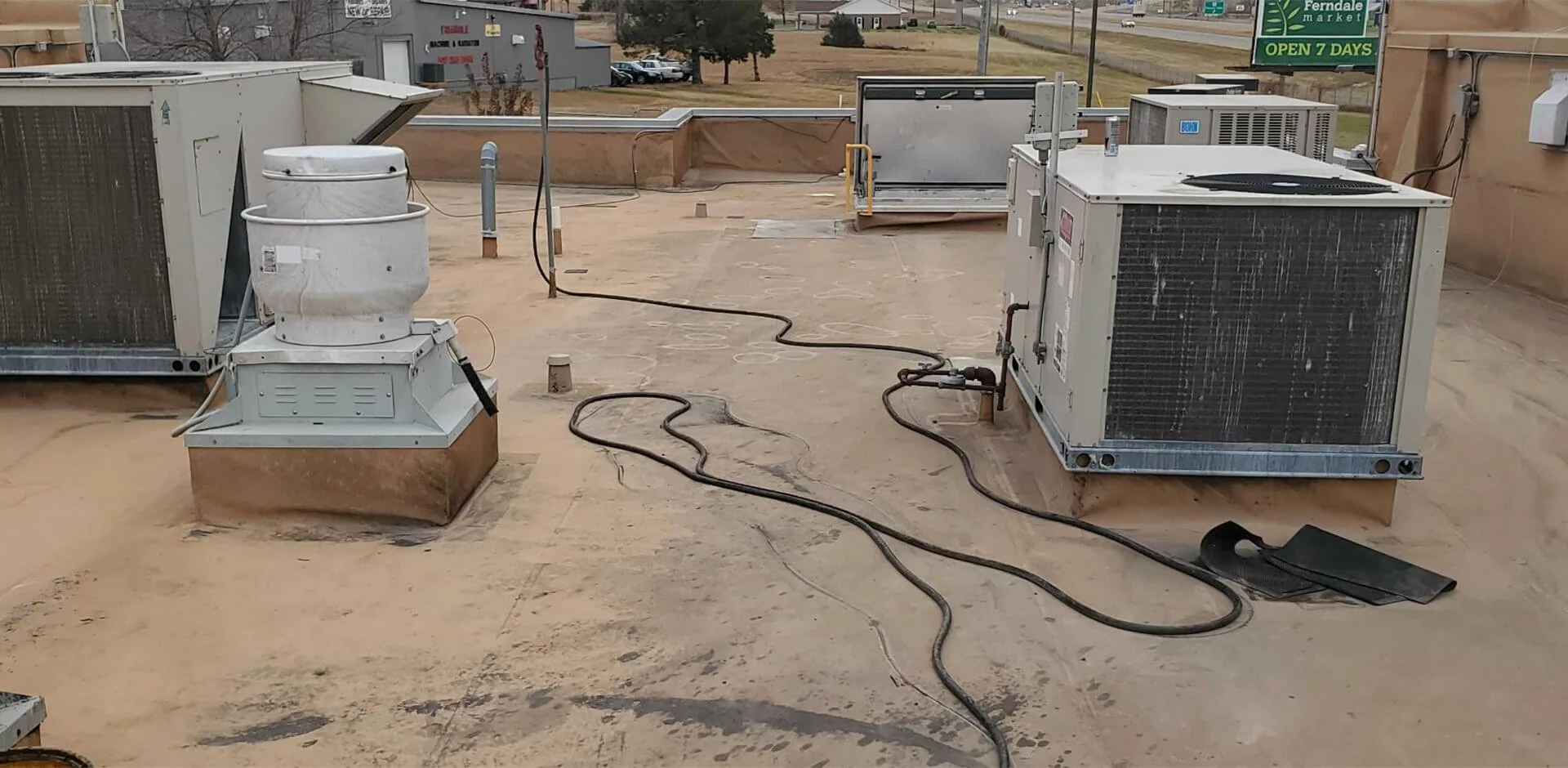 A weathered tan commercial roof crowded with rooftop units before reroofing