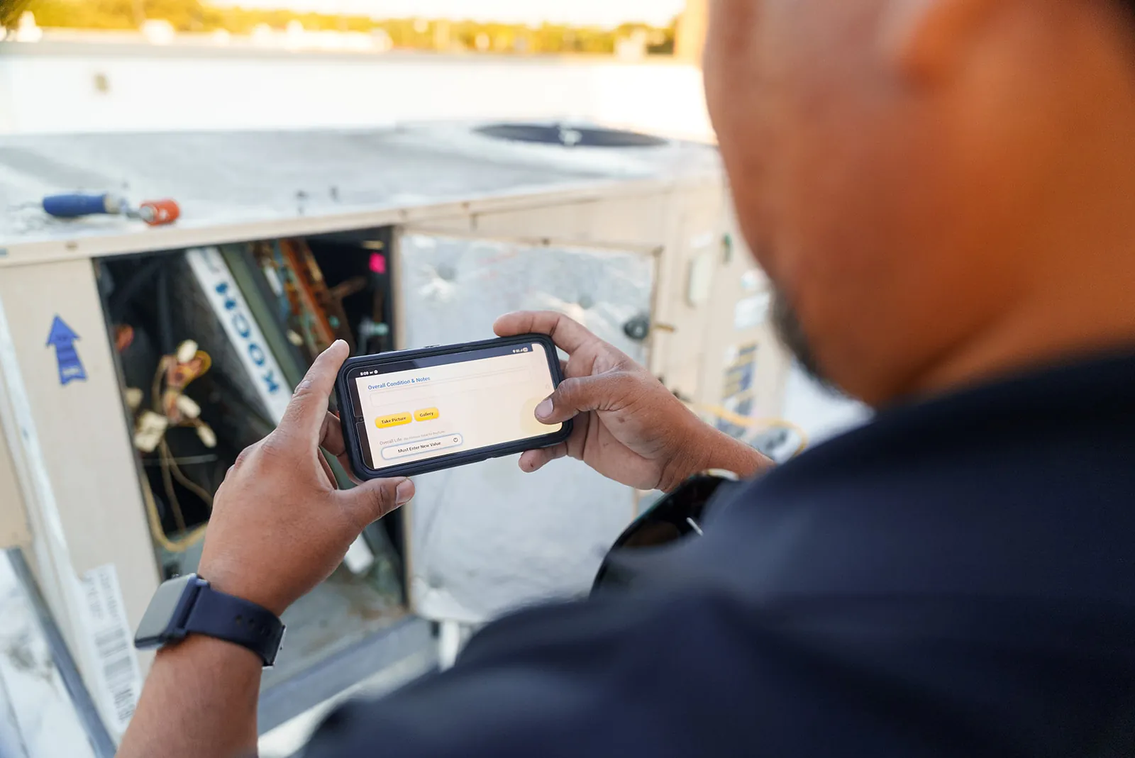 A Field Advisor recording findings on a handheld device at a rooftop unit