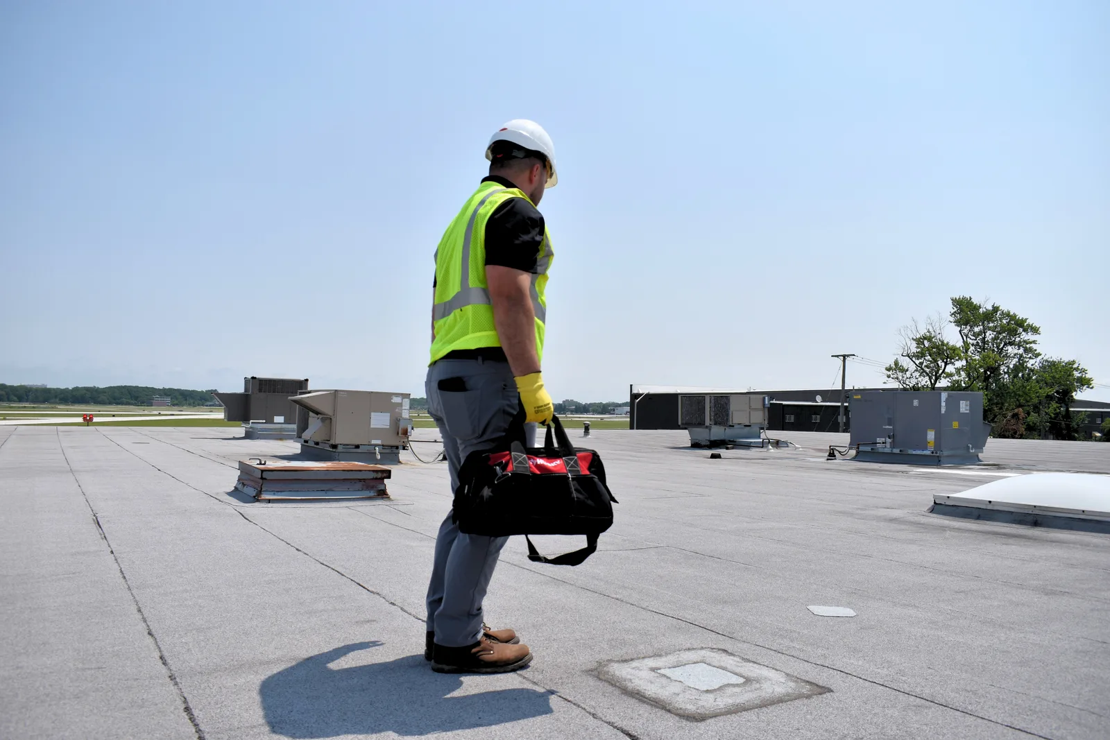 A Field Advisor walking away across a commercial roof with a tool bag
